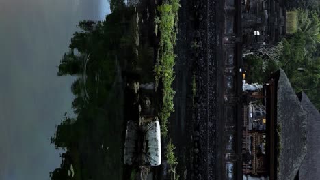 Vertical-slow-motion-static-shot-of-a-pond-in-the-sacred-pura-tirta-empul-temple-with-view-of-the-temple-buildings,-flying-birds-and-water-plants-in-ubud-on-bali-indonesia