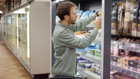 man in shirt walking with a cart through the supermarket choosing and taking groceries in refrigerator