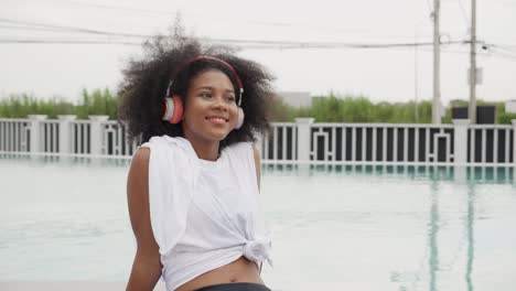 young african american woman wearing headphones listening music at swimming pool, female wearing earphones while enjoy with happiness at poolside, emotion and feeling, lifestyles concept.