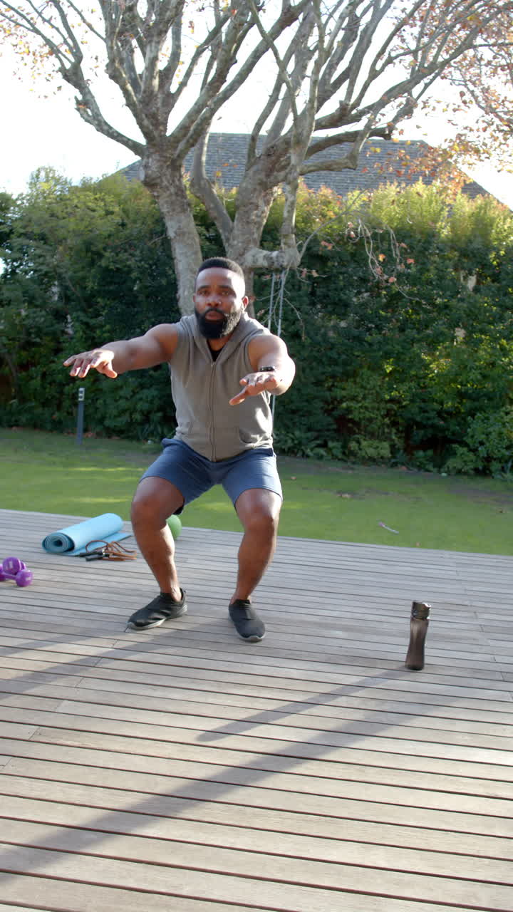 Vertical video of african american man fitness training exercising on deck in garden, slow motion