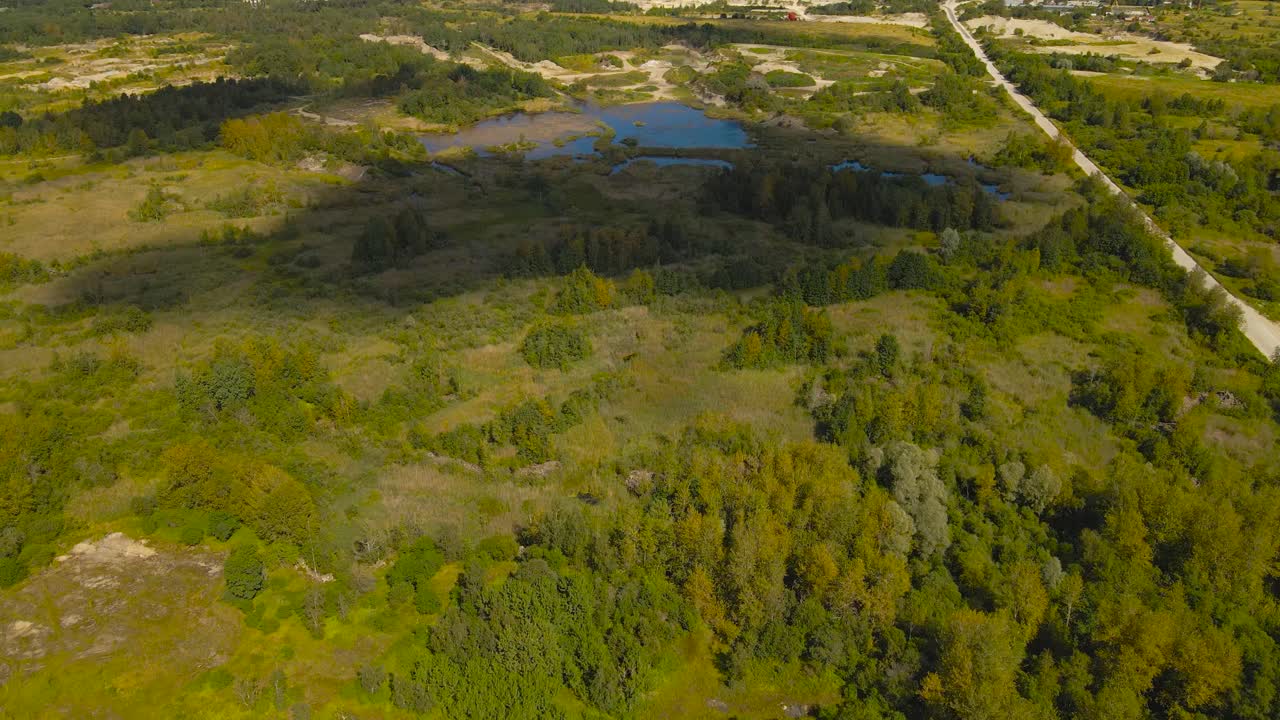 Aerial drone video flying above a large former limestone quarry area that has regrown and what has a large blue colored lake where cloud shadows go over slowly during a sunny summer or autumn day