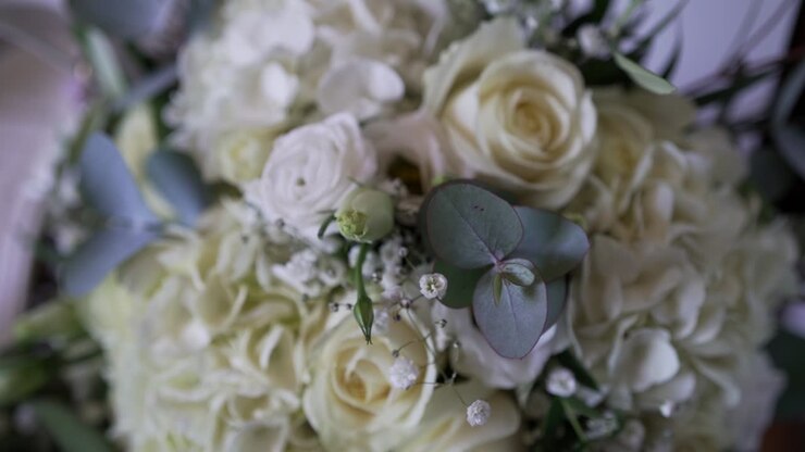 Close up of elegant white bridal bouquet with roses ranunculus baby breath and eucalyptus leaves soft romantic wedding detail