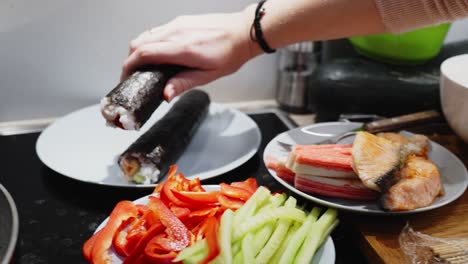 persona que sostiene un rollo de sushi verde para colocarlo en un plato blanco, preparación casera