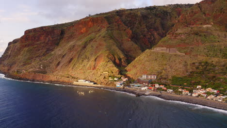 aerial view of gigantic cliff wall and small located village on the ocean shore during sunny day