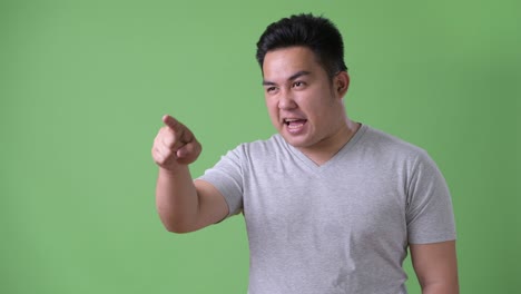 young handsome overweight asian man against green background