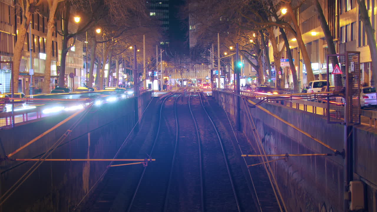 Timelapse with symmetrical arrangement of trams and traffic at the train station. Trams smoothly enter and exit while cars flow on the side. Tracks in the foreground provide a visual focal point.