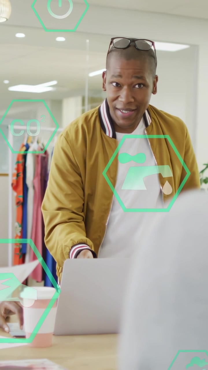 Lead leaning over laptop and speaking, guiding studio review with green hexagon overlaying laptop