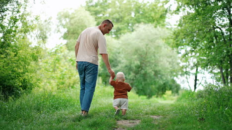 dad leading his lovely little baby boy by the hand. father and toddler son on the walk in summer.