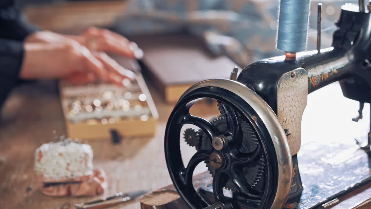 Handmade sewing machine on the table on the background of tailor's hands in workplace. Old black sewing machine and a seamstress nearby in atelier. Retro sewing machine.