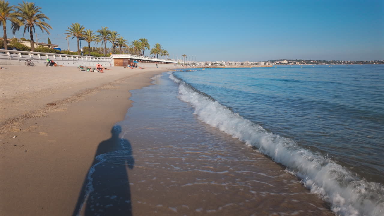 View of waves washing up on sandy shore with a man's shadow visible