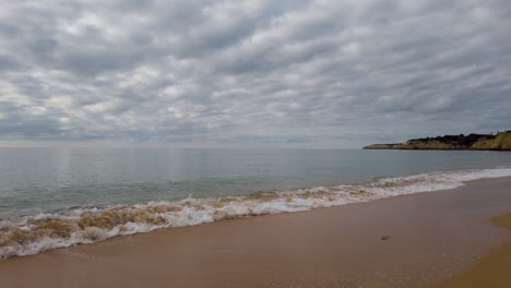 Vista-Del-Océano-En-Una-Playa-De-Arena-Y-Costa-Rocosa-En-La-Distancia