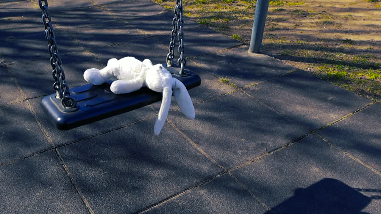 Trist glemt hvit kosedyrkanin som svinger helt alene på en tom huske på en øde lekeplass, som symboliserer ensomhet, tapt barndom, forsømmelse og forlatthet