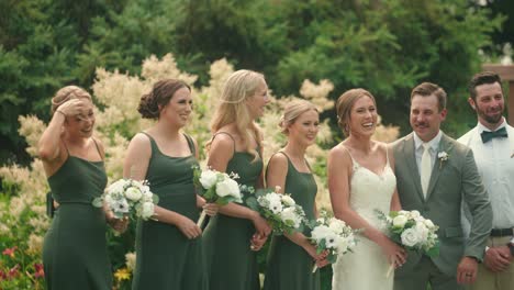 bridal party laughs and jokes together in garden while camera pans in slow motion