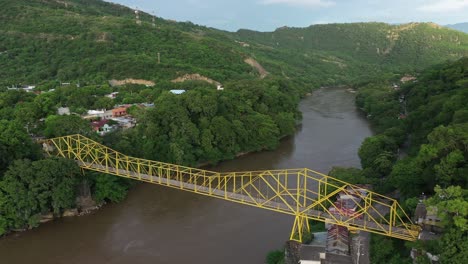 drone aerial view, yellow bridge above muddy magdalena river in green landscape of colombian highlands near honda town, tolima region, revealing shot