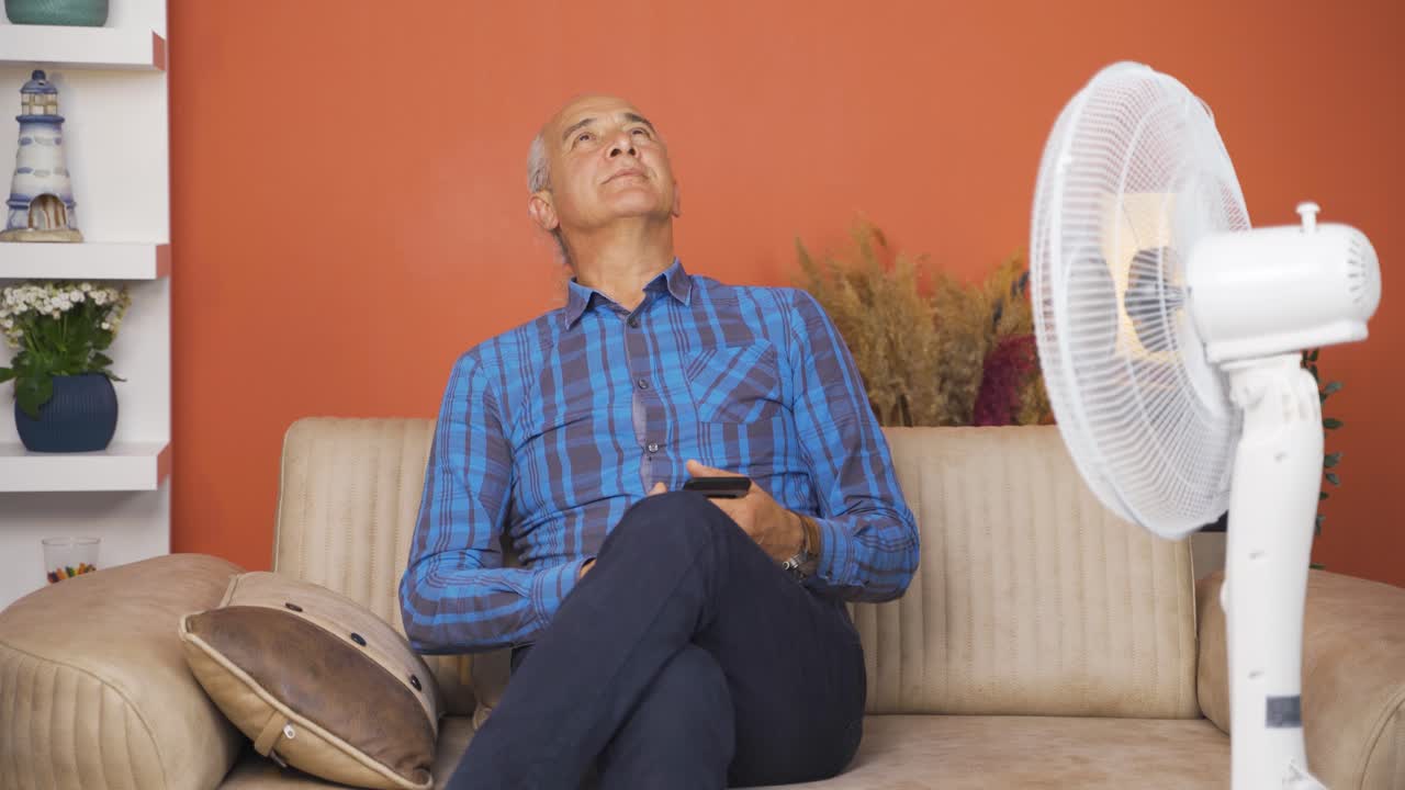 el anciano abrumado por el aire caliente se enfría con el ventilador.
