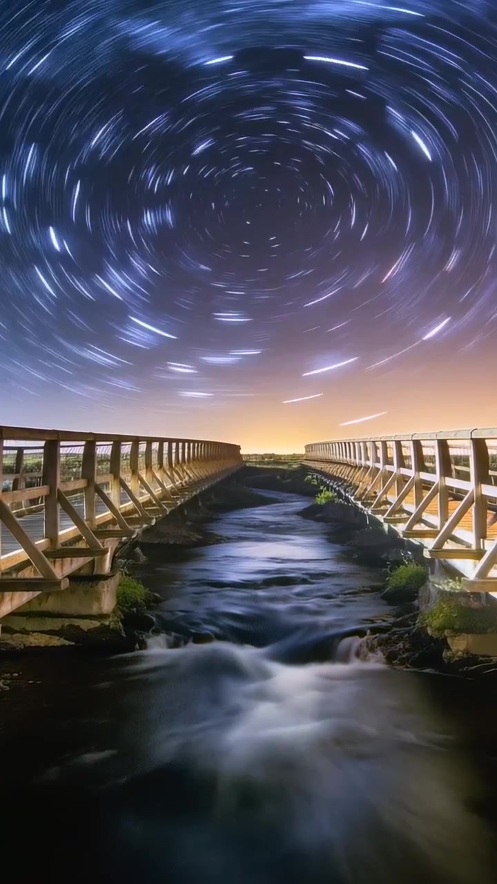 Video verticale: Avvio di una astro-camera che filma un ponte con ringhiera e un canale di notte, registrando la rotazione delle stelle.