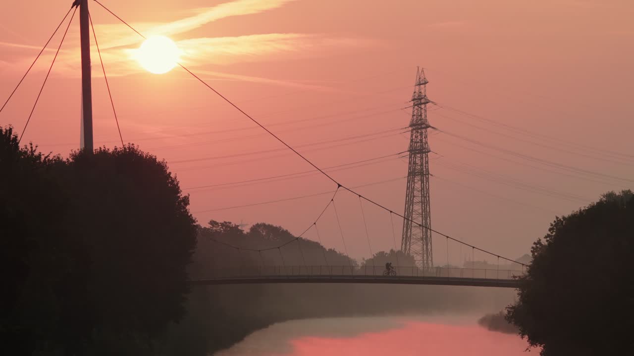 Silhouette of  cyclist crossing suspension bridge at dawn, Gelsenkirchen Germany