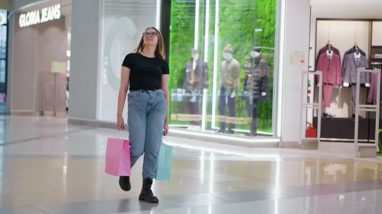 Sikker kvinde, der går i et indkøbscenter med farverigt tøj udstillet på mannequiner og lysende butiksskilt i baggrunden, hvilket afspejler en livlig detailhandelsstemning og forbrugeradfærd.