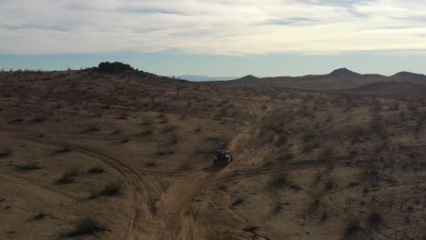 an all-terrain vehicle climbing a incline to a high plateau in the mojave desert and a view of the surrounding rugged terrain - aerial view