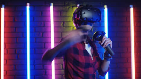 young woman in vr glasses and using joystick while playing a virtual reality game in a room with colorful neon lamps on the wall 5