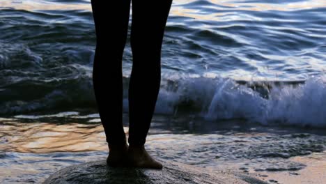 Low-section-of-woman-performing-yoga-on-the-beach