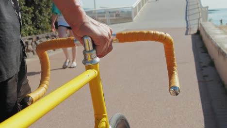 person holding yellow fixed gear bicycle on a beach path