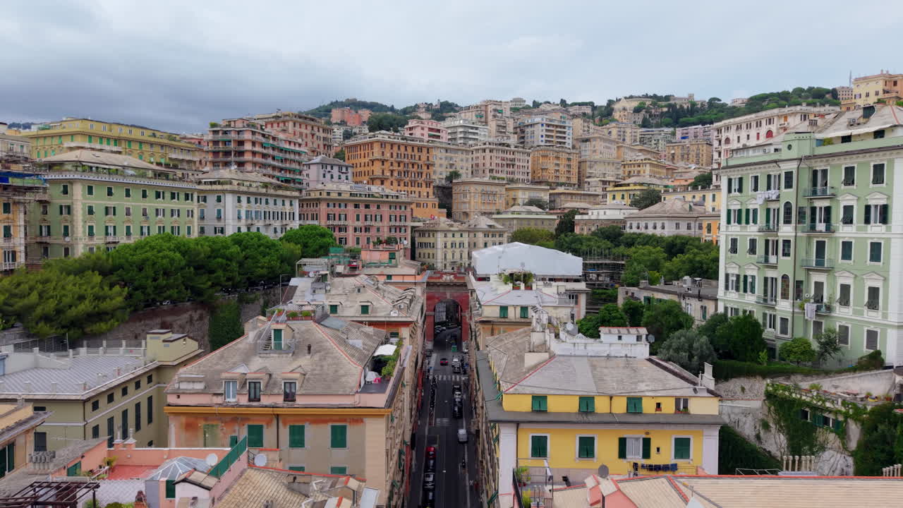 The drone flies backward above the colorful rooftops of Genoa, showing a red bridge and the hillside buildings of the city