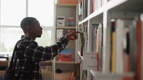 man seeks book on shelf in library. african american student chooses literature for homework making in university information center. guy in bookstore