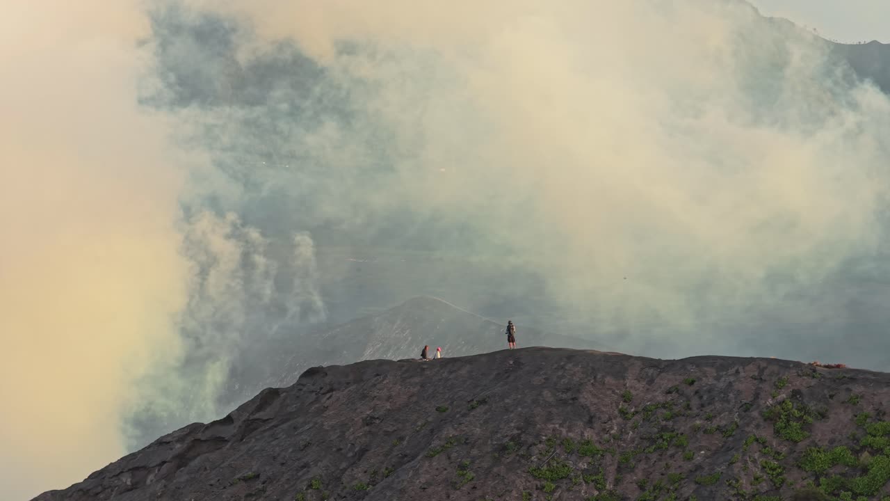 Gente en el borde del cráter del Monte Bromo con humo volcánico
