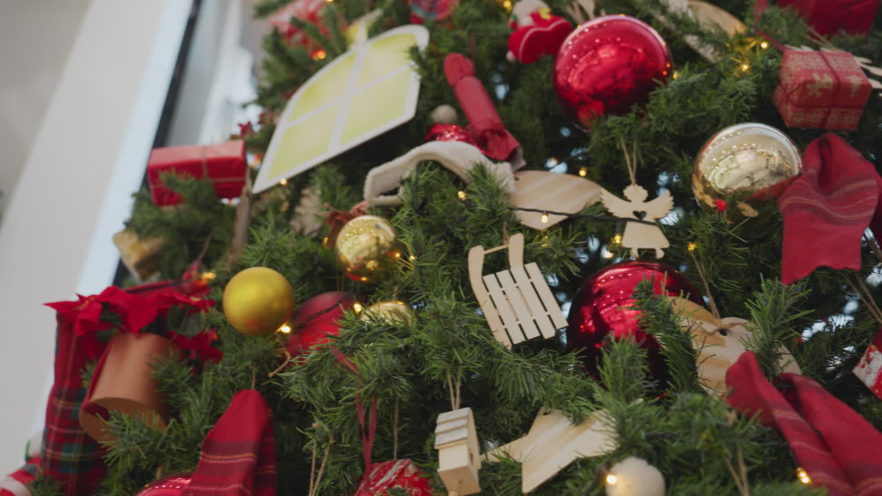 Close-up of beautifully decorated Christmas tree with red and gold ornaments, wrapped gift boxes, Santa Claus figure, wooden stars, and festive ribbons glowing under warm lights in a shopping mall