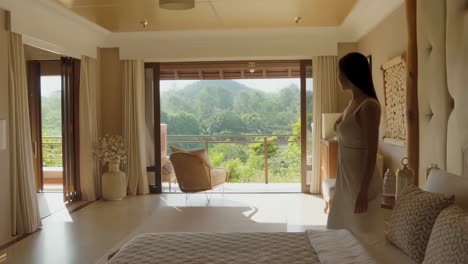 a woman walks towards a balcony with a scenic view in a luxurious room