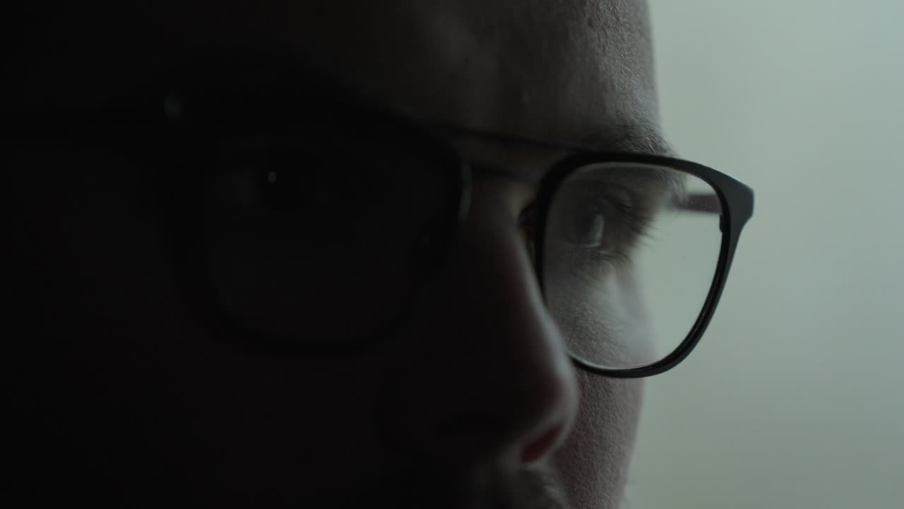 Primo piano con effetto soft focus dell'occhio di un uomo dietro gli occhiali vicino a una finestra in penombra, per creare un'atmosfera di tensione e introspezione. Ideale per concetti come ansia, affaticamento, privacy, sorveglianza e psicologia.