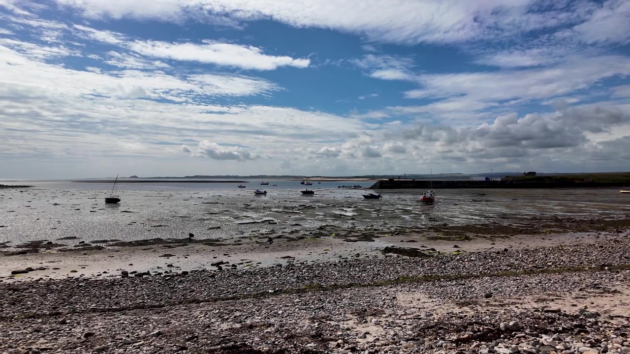 Barche ormeggiate si trovano sulle distese di fango esposte del Mare del Nord al largo di Holy Island, mentre la telecamera panoramica lentamente attraverso l'ampia baia e il cielo.