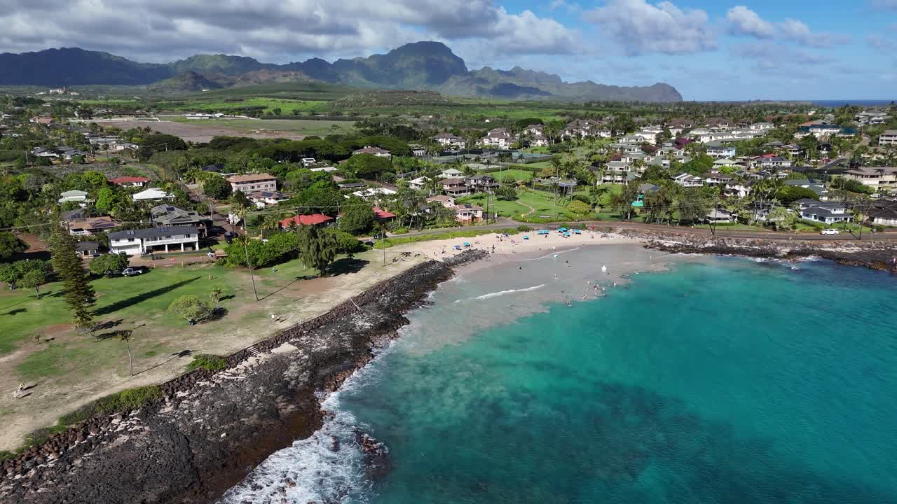 Vista aerea con drone di Kauai, Hawaii, con spiaggia di sabbia e acqua di mare cristallina e montagne sullo sfondo, meta di viaggi e vacanze