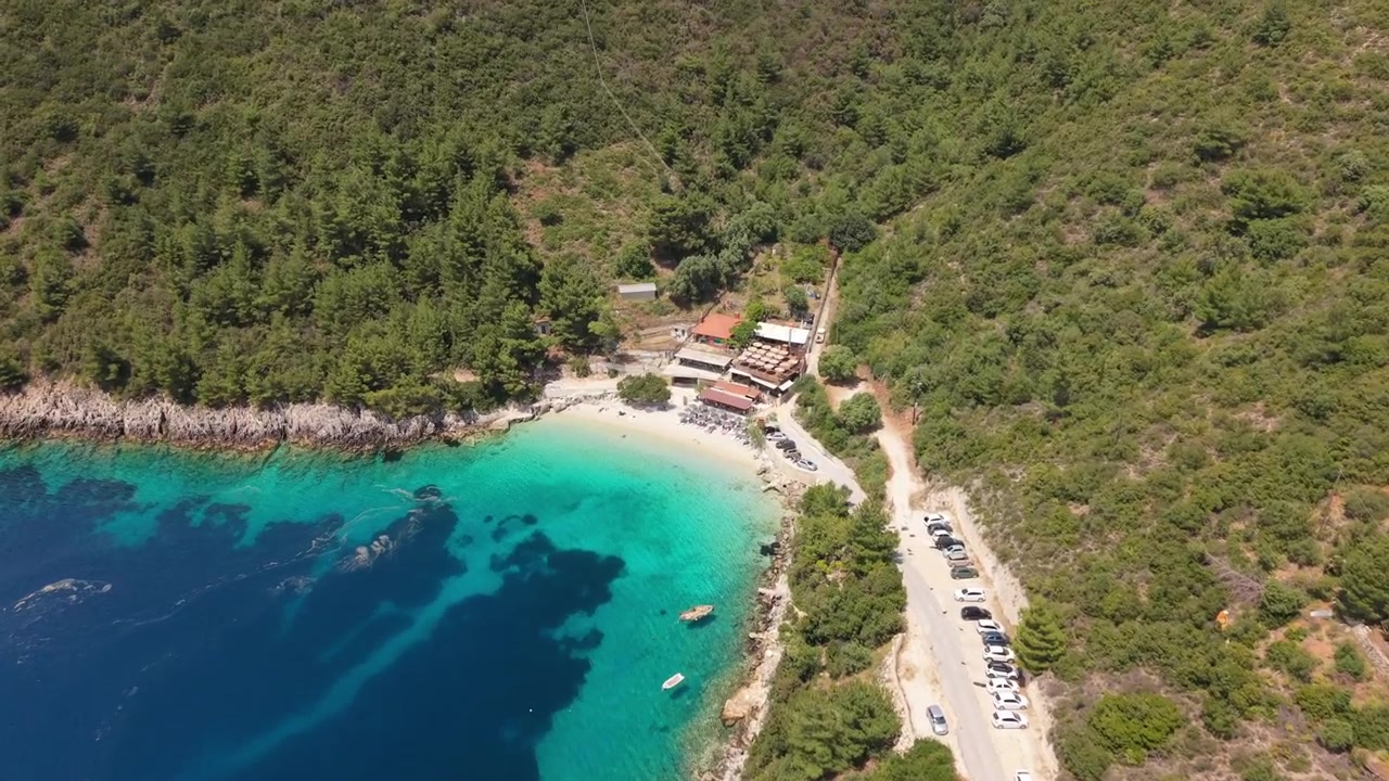 Volo di drone sulle acque cristalline della spiaggia di Afteli sull'isola di Lefkada, Grecia. Baia panoramica con mare turchese, colline boscose, strada costiera e un'atmosfera estiva mediterranea e pacifica.