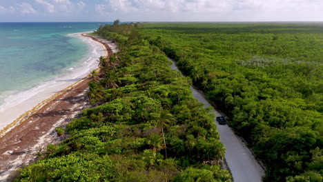 Amplia-Toma-De-Un-Dron-De-Un-Auto-Conduciendo-A-Lo-Largo-De-La-Costa-Natural-Cerca-De-Mahahual-México-Con-Un-Denso-Bosque-Tropical-Y-Agua-Clara-Del-Océano