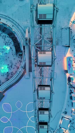vertical flyover top-down drone shot of the snowflake ferris wheel at the harbin ice festival at sunset, china