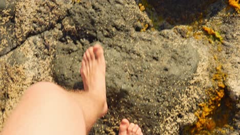 pov shot of man and woman walking bare foot on rocky coast beach, high angle