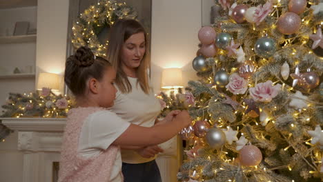 la bambina e la donna decorano l'albero di natale con palline, luci e ornamenti