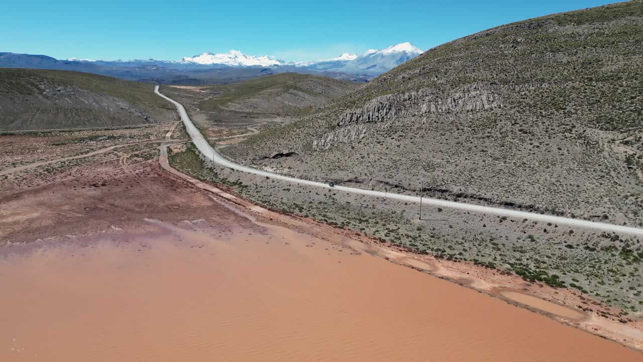 un motociclista solitario viaja por un camino de tierra más allá de una laguna fangosa en las estribaciones de los andes.