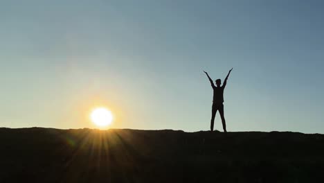 hombre con silueta levanta los brazos, haciendo ejercicio, cansado después de correr, brillante puesta de sol detrás