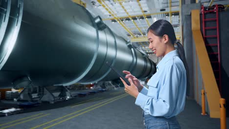 vista lateral de una mujer de negocios asiática usando una tableta en una fábrica de fabricación de tubos