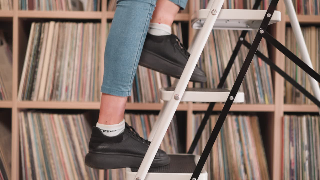 Woman goes up step ladder near bookcase closeup. Librarian uses foldable stairs to take books from upper shelf in library. Student works in bookstore