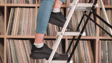 a woman reaches for something on a high shelf using a step ladder