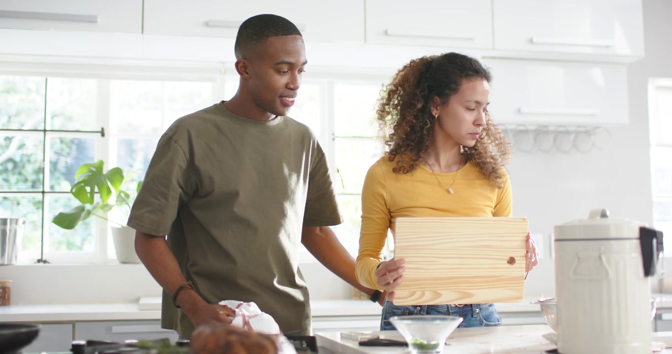 Diverse couple cooking at kitchen island, woman inspecting bowl and moving wooden board to sink