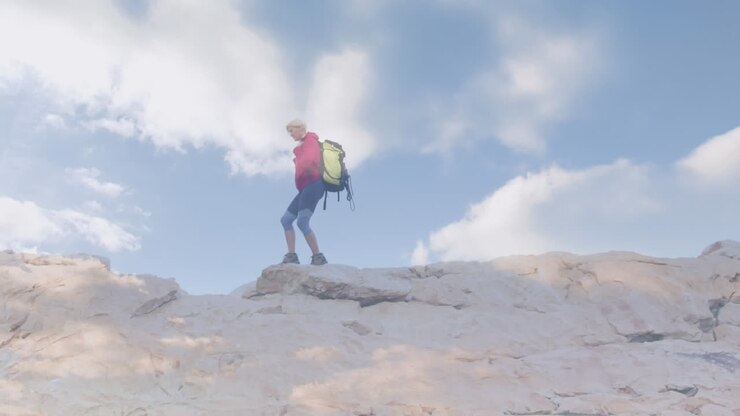 Felice donna anziana caucasica che fa escursioni in montagna, su nuvole in rapido movimento