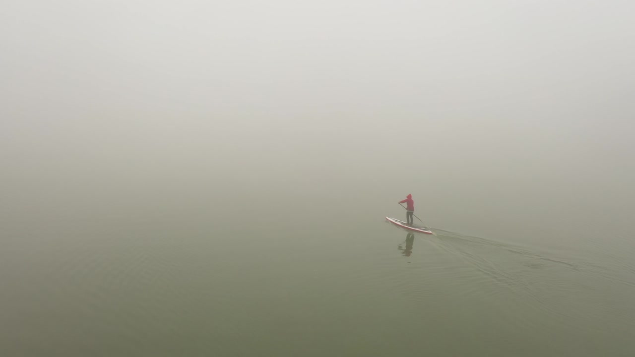 одинокий человек плывет на доске по реке в очень густом тумане