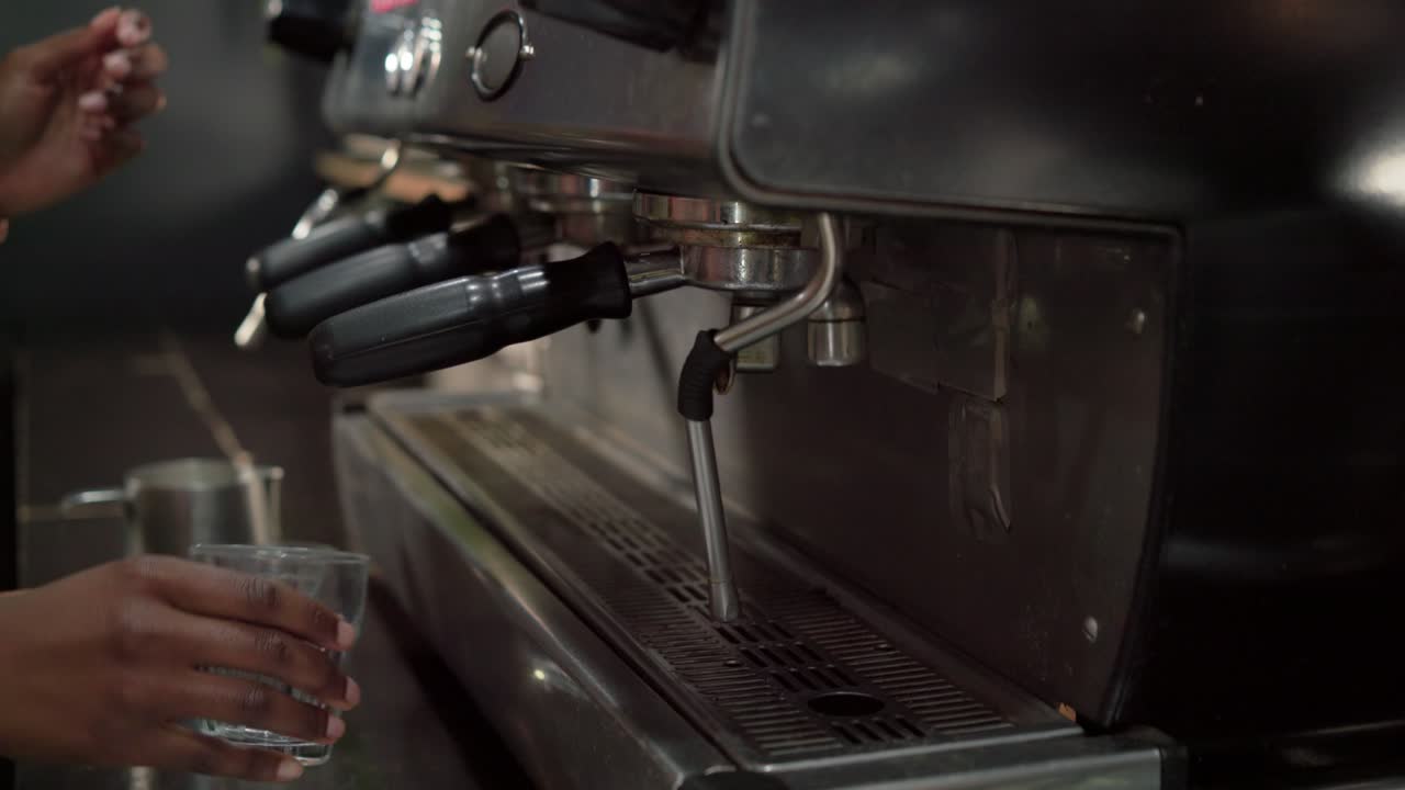 Barista afroamericana che lavora in un bar, mentre inserisce un portafiltro nella macchina e prepara un caffè per un ordine