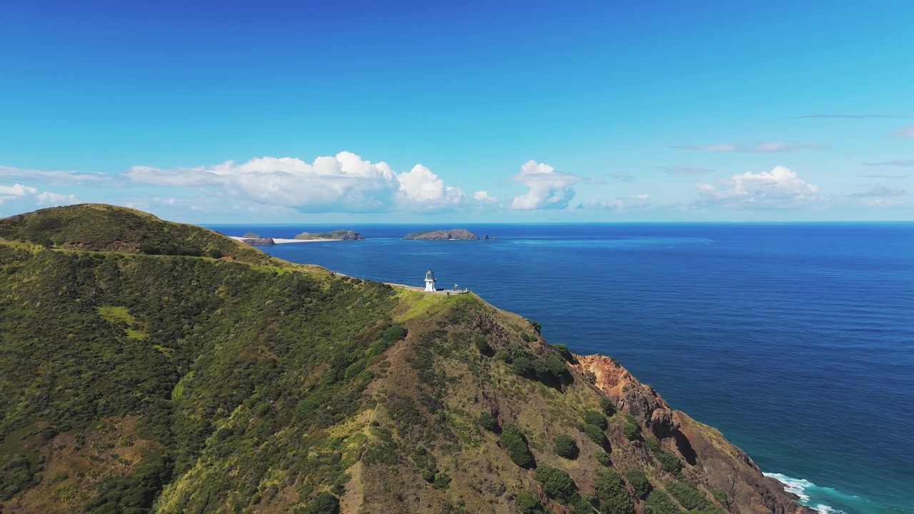 Aerea: Faro di Cape Reinga, Mar di Tasman e Oceano Pacifico di giorno a Cape Reinga, Nuova Zelanda, ripresa con drone in allontanamento.