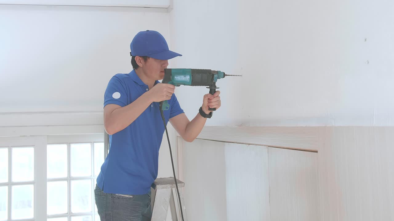 hombre asiático técnico trabajador en una escalera uso taladro eléctrico en la pared